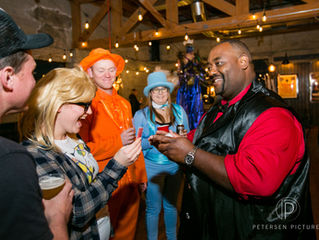Costumed partygoers laugh with a smiling magician at a warm indoor party; Petersen Pictures watermark visible.