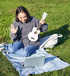cheerful-asian-girl-musician-waves-at-her-laptop-say-hi-to-video-chat-plays-ukulele-and-re