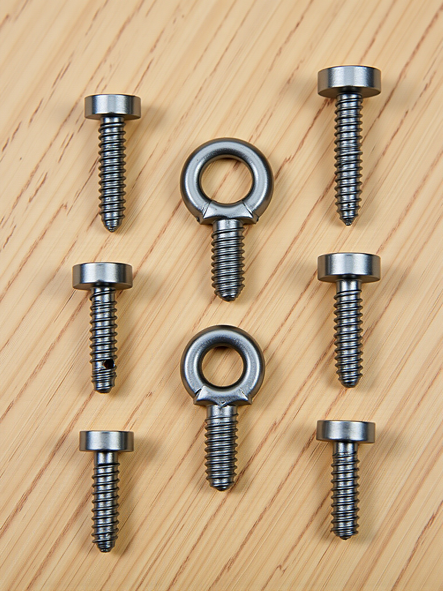Tornillos de metal y dos tornillos de ojo sobre superficie de madera clara.