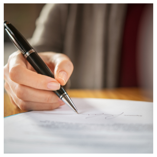 Hand signing a real estate agreement with a pen at a wooden table.