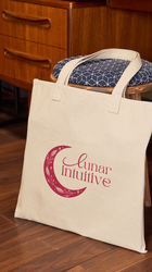 lunar intuitive moon and text logo on a tote bag on the ground in front of a stool