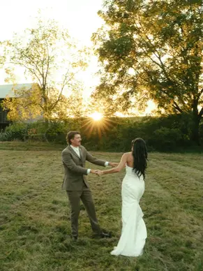 Bride and groom in a field dancing with the sun setting behind them