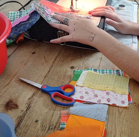 girl sewing on sewing machine with pile of scrap fabric on a table next to her