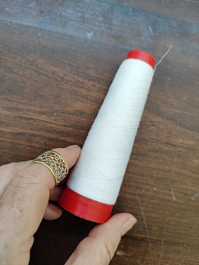 hand holding spool of white thread