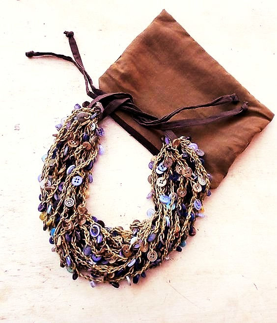 Thumbnail: tan and ocean button necklace draped over a brown zippered pouch