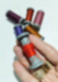 a hand holding a spool of orange sewing thread in front of 5 other spools lying on a table