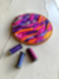 slow stitch sunset art quilt in a wooden hoop with 3 spools of colored sewing thread on a table