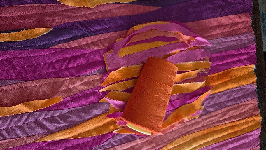 spool fo orange thread strips of fabric for a sun laid out on a wave landscape patchwork background