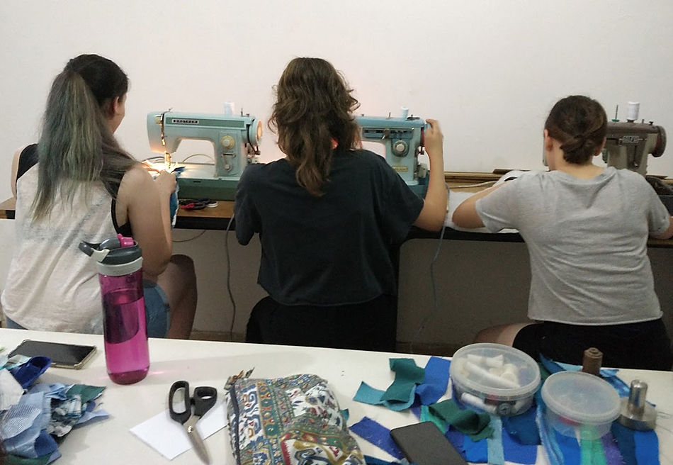 3 teenage girls sewing on vintage sewing machines with fabrics on a table behind them