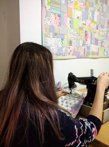 Gilrs sewing on a vintage sewing machine with a patchwork quilt on the wall