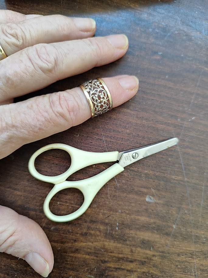 very small pair of scissors nect to a hand for size on a table