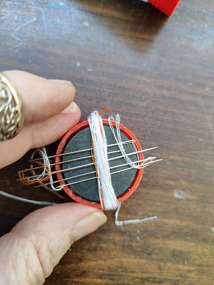 hand holding small magnet with needles and threads