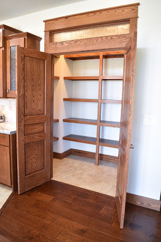 Walk-in pantry with wood shelving and transom above french doors.