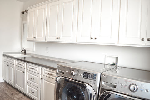Modern laundry room with lots of white cabinets, a utility sink, and washer/dryer.