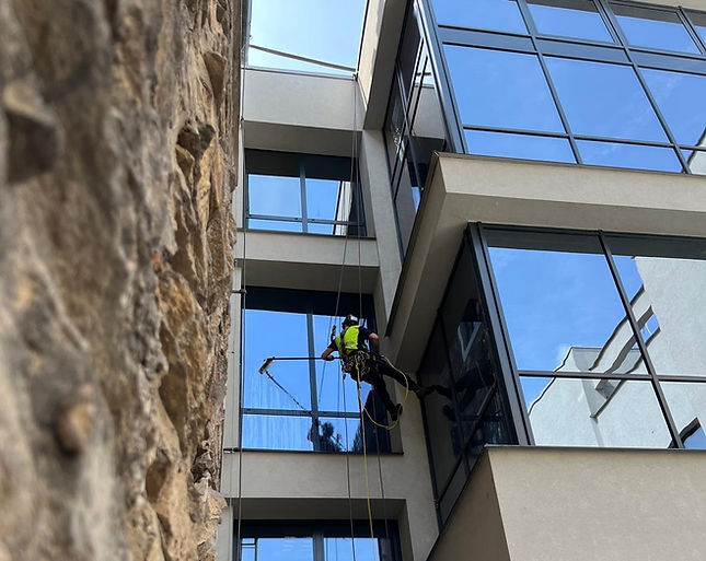 Pracovník ve výškých myje fasádu demiralizovanou vodou.