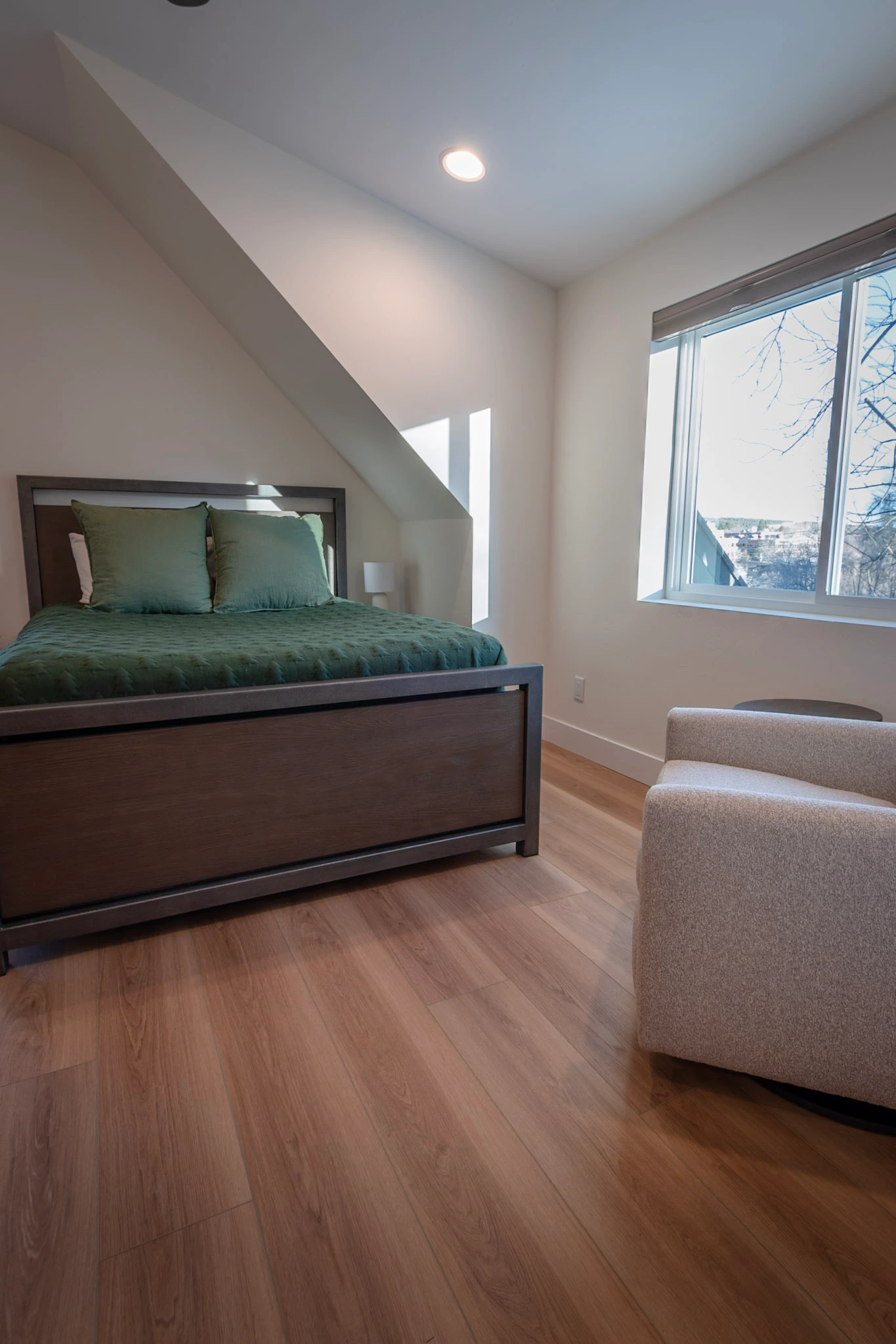 Bedroom with wooden bed, green bedding, and armchair.