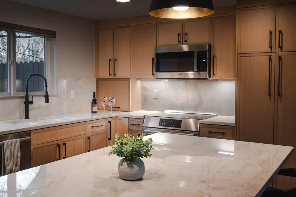 Kitchen remodel with medium tone wood cabinets, dark hardware, white and gray marbled countertops.