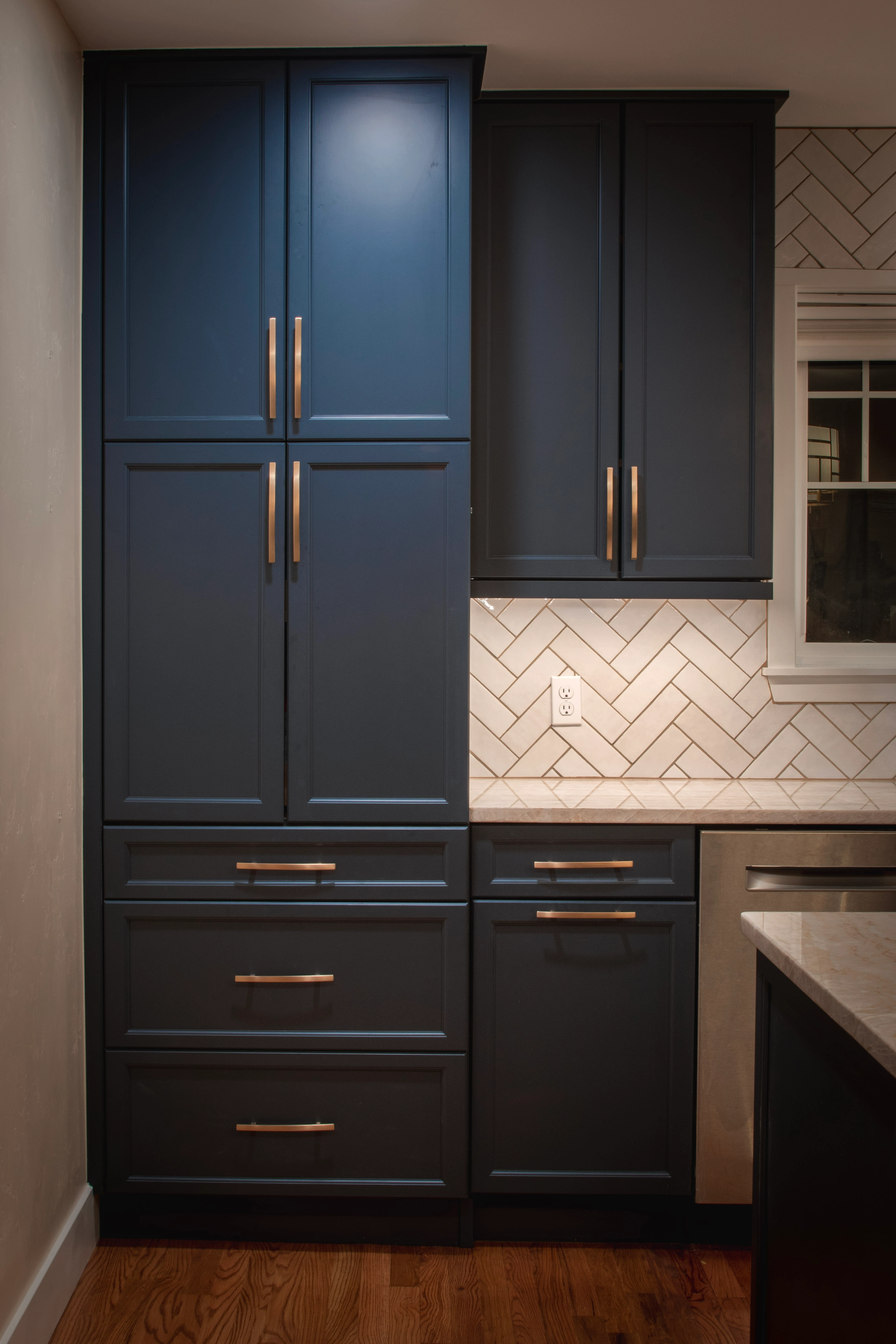 Navy blue storage cabinets with a tall pantry and gold handles