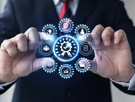 Hands in a suit hold a holographic interface with icons like a globe, people, and a checkmark. Blue tones, tech-themed setting.