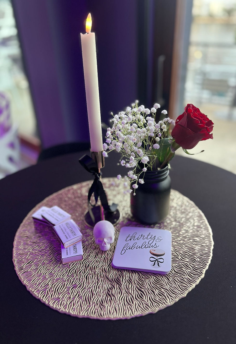 Moody black vases and painted mason jars filled with red roses and baby’s breath centerpieces, accented with white skull décor for a Death to My 20s birthday celebration.
