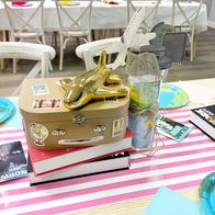 Travel-themed party centerpiece with small suitcase, passport stamps, and travel books