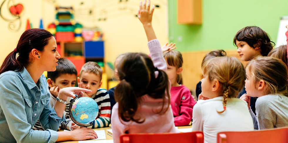 Teacher with a globe engages kids in a colorful classroom. One child raises their hand, showing curiosity and focus.