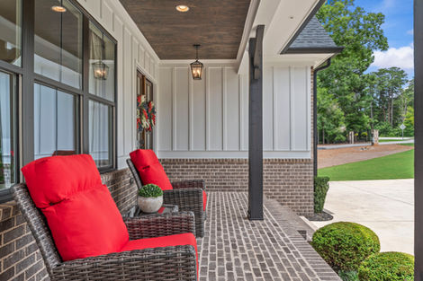 Covered brick front porch with wicker seating and red cushions