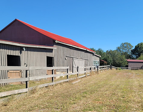 a field with a barn, fence, and trees in the background