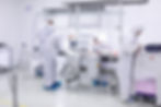 People in white hazmat suits working in a cleanroom, inspecting items on a conveyor belt. Bright, sterile environment with a focused mood.