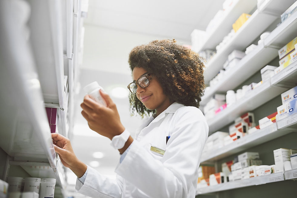 Pharmacist in a white coat examines a bottle on a shelf in a well-lit pharmacy. Shelves filled with colorful medicine boxes.