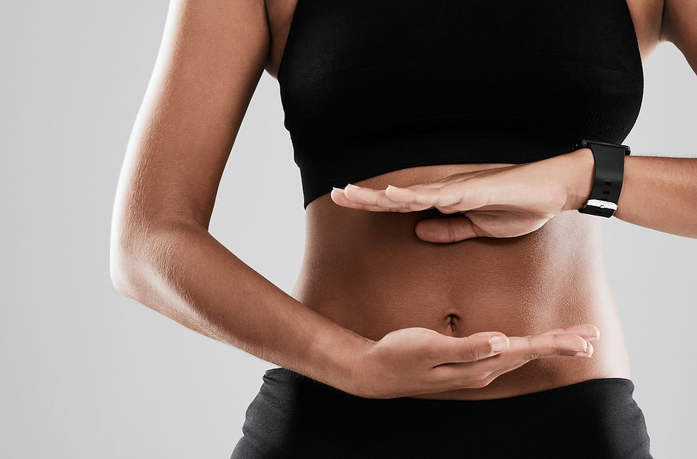 Person in black sportswear holds hands in a parallel gesture over a toned stomach. Gray background. Mood is calm and focused.