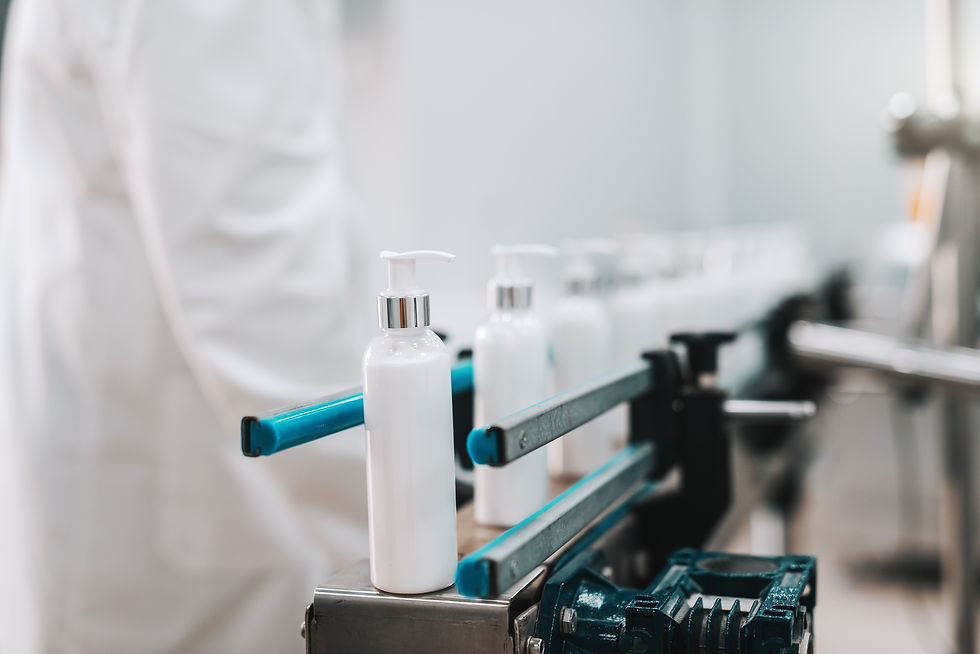White pump bottles on a conveyor in a factory setting, with a person in a white coat blurred in the background.