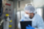 Technician in safety gear inspects machinery, holding clipboard. Stainless steel equipment and control panel with buttons in the background.