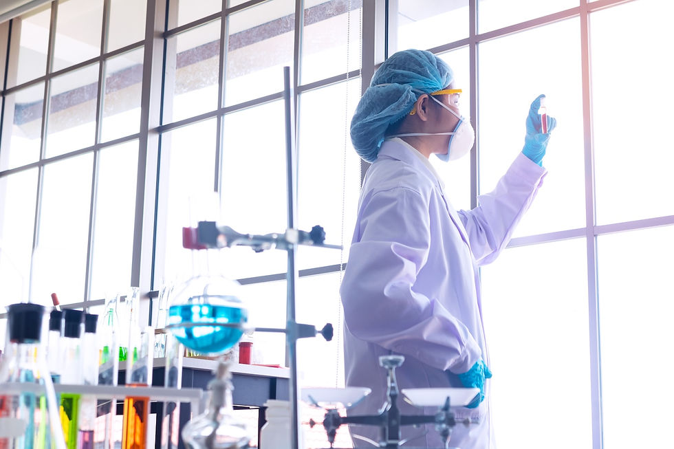 Scientist in a lab coat examines a test tube by a large window. Lab equipment with colorful liquids surrounds them. Bright, clinical setting.