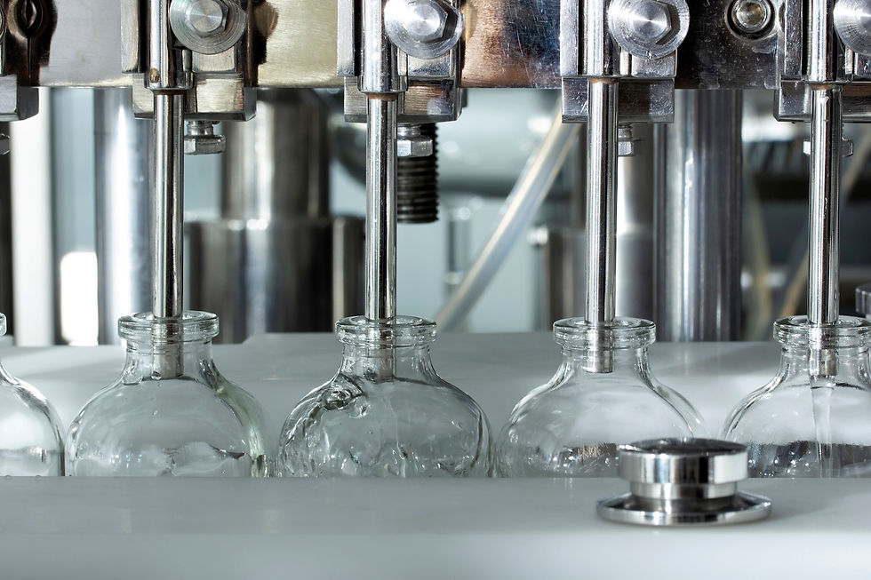 Glass bottles being filled by metal nozzles on a factory production line. The setting is industrial with a clean, metallic ambiance.