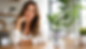 Smiling woman sits at a wooden table beside a LIFT supplement bottle in a bright, plant-filled room.
