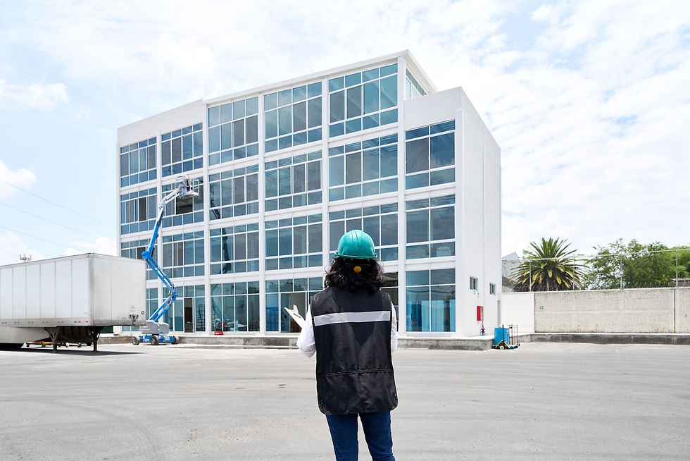 Person in a hard hat observes a worker on a lift cleaning windows of a modern office building. Bright and sunny day with a few clouds.