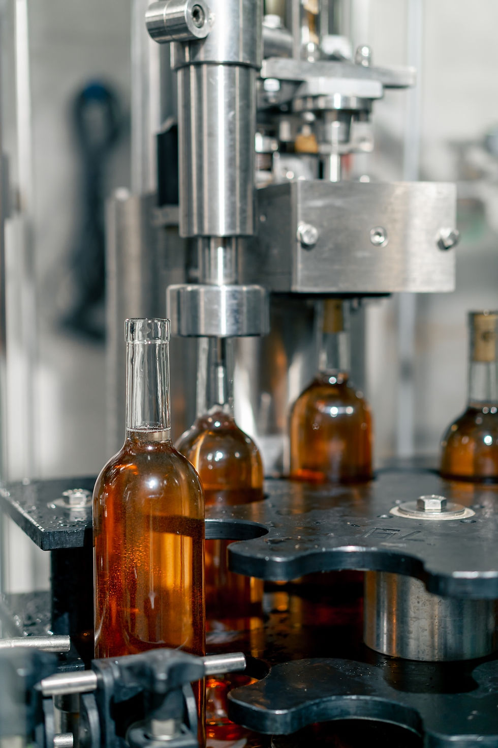 Machines fill amber bottles with liquid on an industrial bottling line. The scene has a metallic and industrial setting.