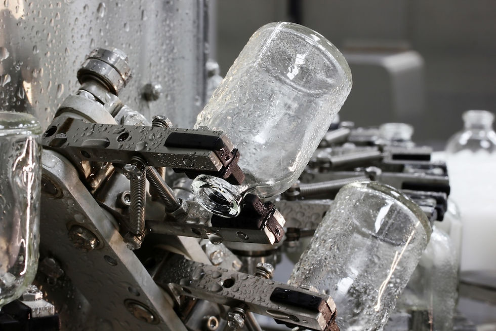 Glass production line with wet jars held by metal clamps in a factory setting. The machinery is silver, and the jars are clear.
