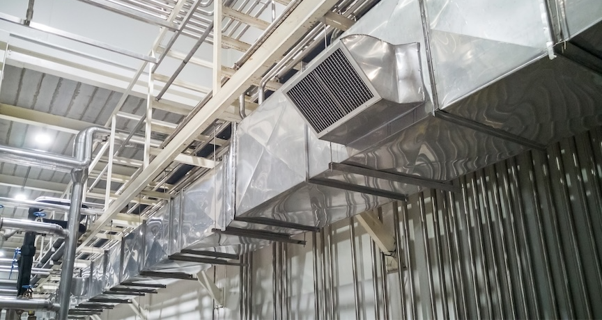 Industrial setting with silver metal ductwork and pipes on a ceiling. Brightly lit environment with no visible text or people.