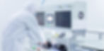 Person in white protective suit operates a machine in a laboratory. The setting is clean and bright, with screens and gauges on the device.