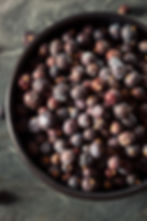 A bowl brimful of dark, dried maqui berries on a textured stone background, highlighting their deep purple hues and rough texture.