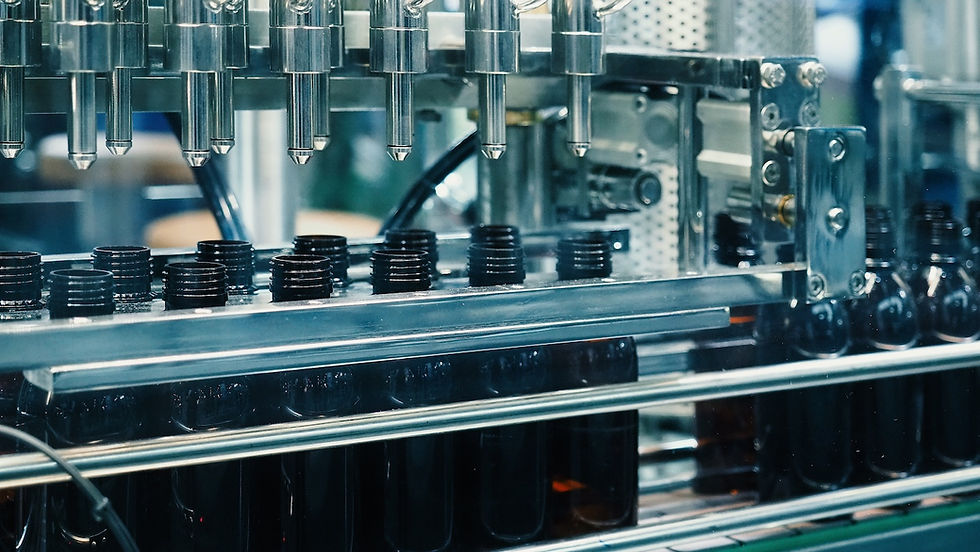 A factory machine fills dark glass bottles in a production line, featuring metallic components and a blurred industrial background.