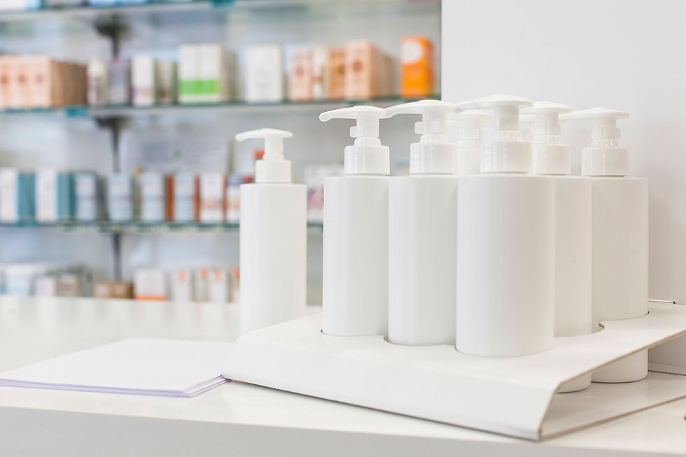 White pump bottles on a pharmacy counter with shelves of products blurred in the background; a stack of papers lies nearby.