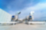 Large industrial ventilation ducts on a rooftop against a blue sky. The setting is bright with a modern, clean structure. No visible text.