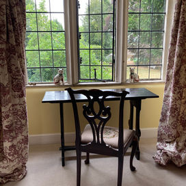 Writing table and chair with latticed windows overlooking a summer garden 