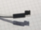 A close-up photo of a 0.1" header on the end of a pair of wires - a small black plastic connector with two pins protruding. On one pin is a small shunt jumper, kept on a single pin not to complete the circuit but to usefully store the jumper.