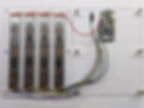 A photo of four slide potentiometers mounted to an acrylic panel, viewed from the underside, showing how the pots are wired to a microcontroller board. Colourful hookup wire is used and small electronic components are visible on the microcontroller board. The microcontroller is an Adafruit Feather RP2040.