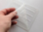 A photo of a hand peeling back the protective film from a clear acrylic panel laser cut with holes for components and screws.