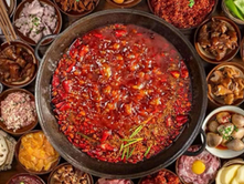 A steaming hotpot filled with red broth in the center, surrounded by various colorful ingredients and small dishes on a wooden table.